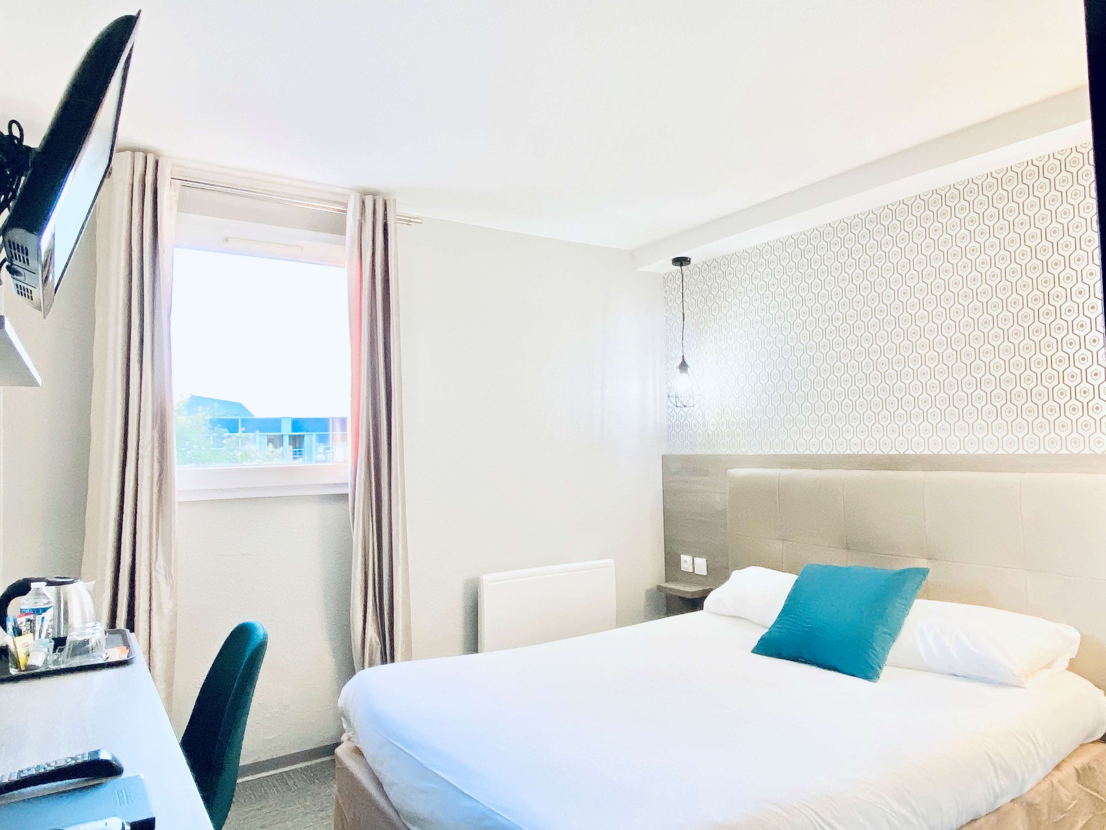 A hotel room with a bed, a desk with a chair, a TV, and a window with curtains.