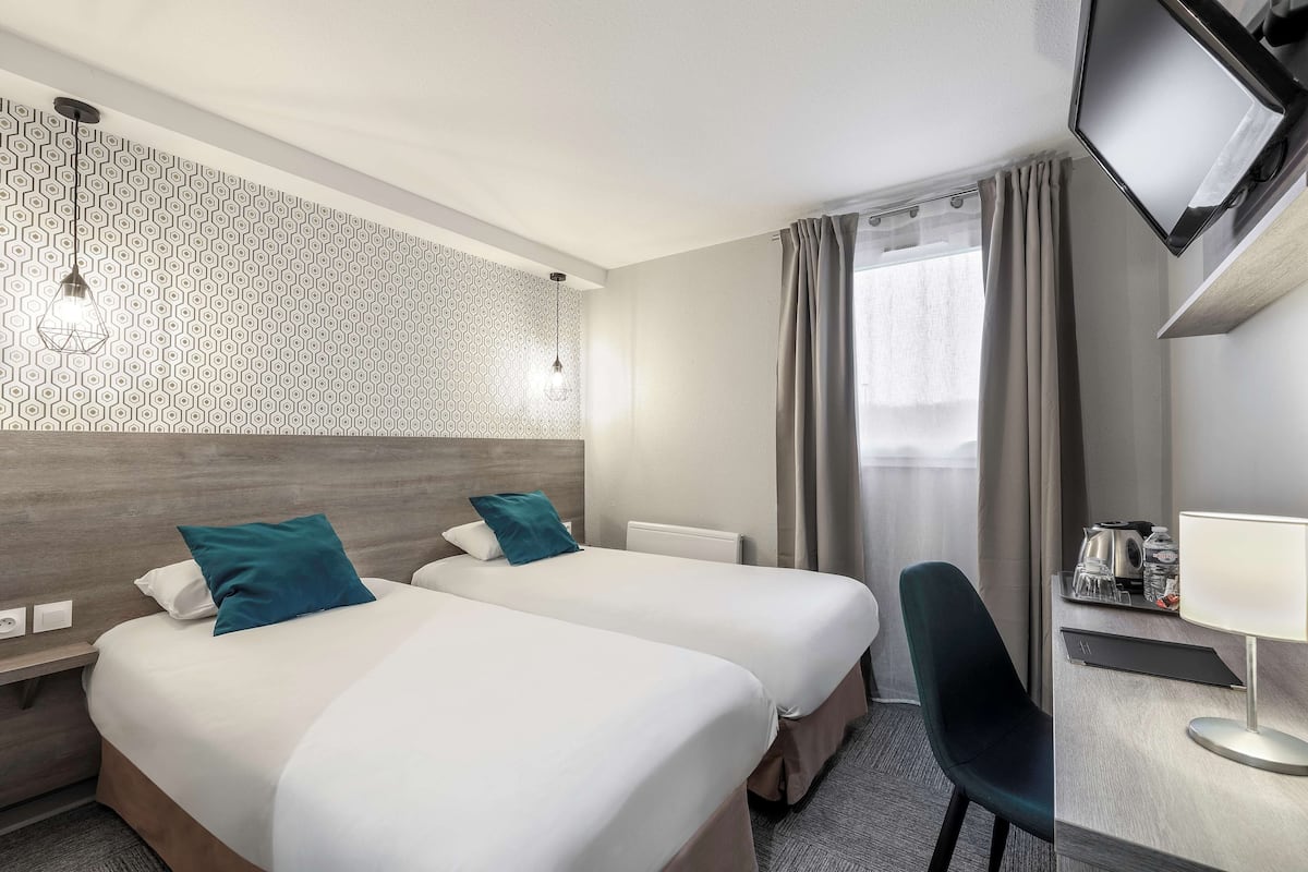 Une chambre d’hôtel avec deux lits, un bureau avec une lampe, une télévision et une fenêtre avec des rideaux.