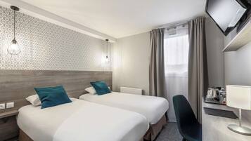 A hotel room with two beds, a desk with a lamp, a TV, and a window with curtains.