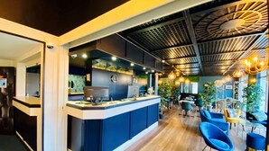 Un espace bar moderne avec un comptoir, un coin salon avec des chaises bleues et un plafond orné d’un motif géométrique.