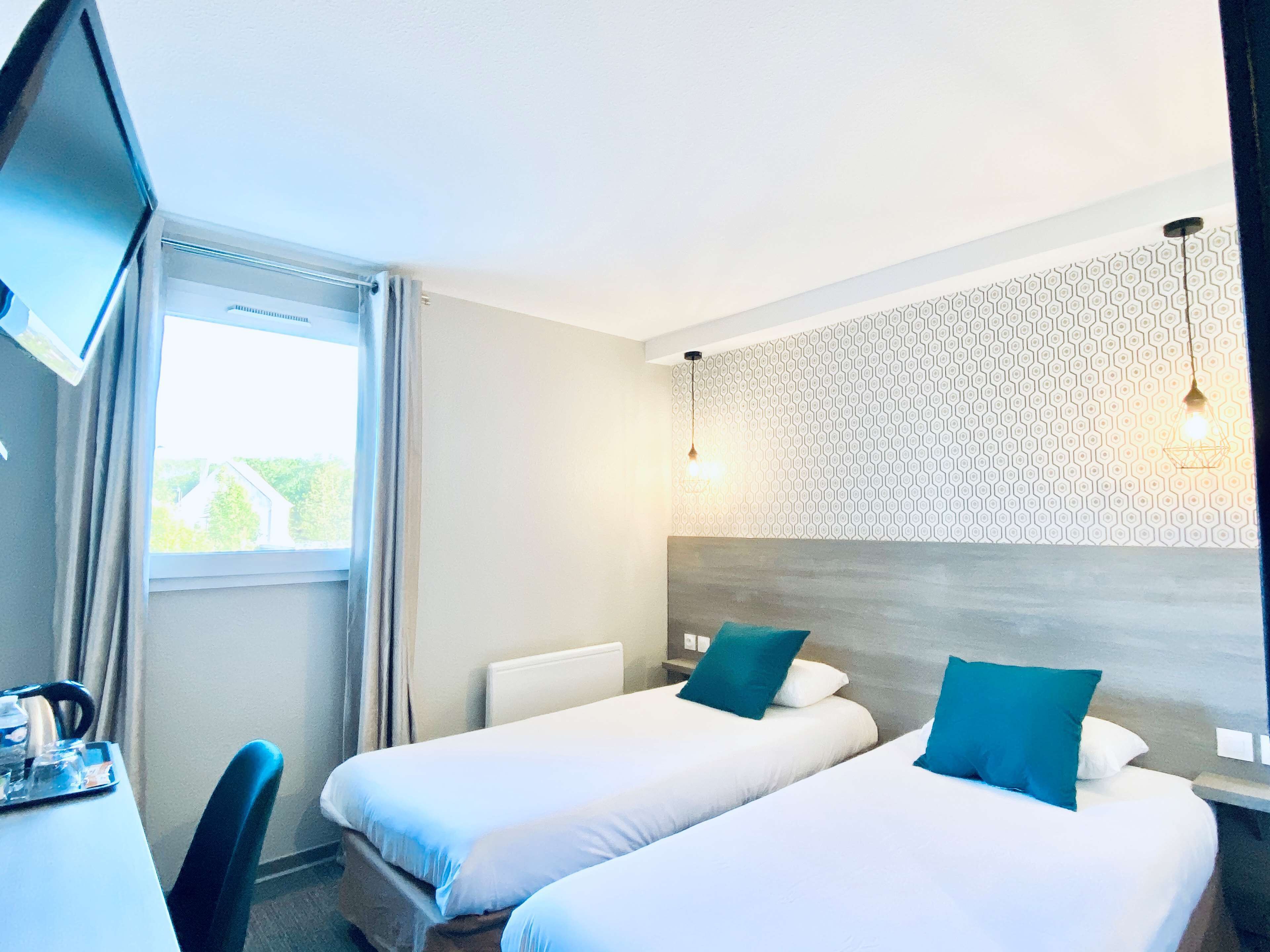 Une chambre d’hôtel avec deux lits, un bureau, une chaise, une télévision et une fenêtre avec des rideaux.
