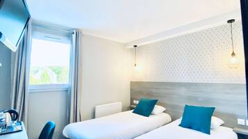 Une chambre d’hôtel avec deux lits, un bureau, une chaise, une télévision et une fenêtre avec des rideaux.