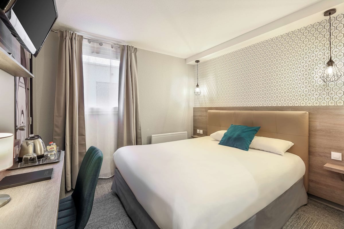 Une chambre d’hôtel avec un lit, un bureau avec une télévision et un mur décoré d’un motif.