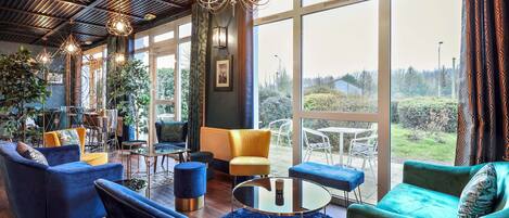 A modern interior with a large window, a chandelier, and blue and green upholstered chairs.