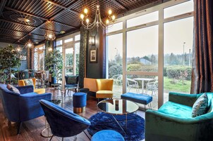 Un interior moderno con un amplio ventanal, una araña y sillones tapizados en azul y verde.