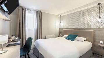 Habitación de hotel con cama, escritorio con lámpara, una silla, televisor montado en la pared y pared con diseño.