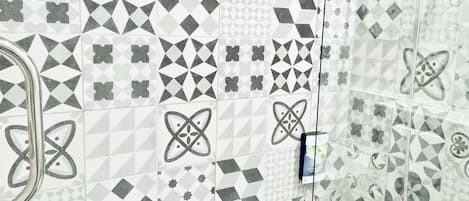 Un baño con una bañera blanca y zona de ducha. Las paredes están cubiertas de baldosas con diversos diseños geométricos y florales.