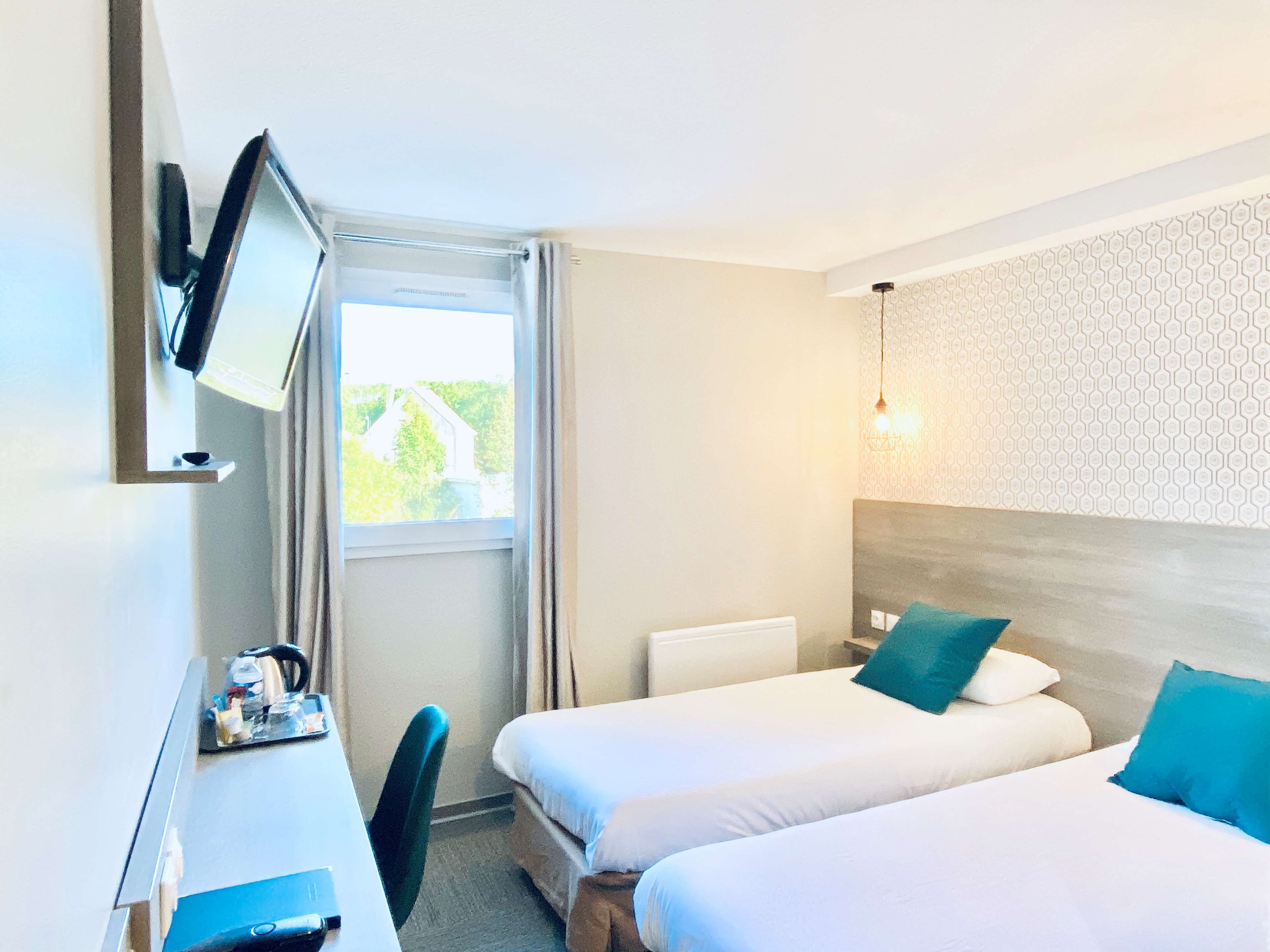 Een hotelkamer met twee bedden, een bureau, een stoel, een aan de muur bevestigde televisie en een raam met gordijnen.