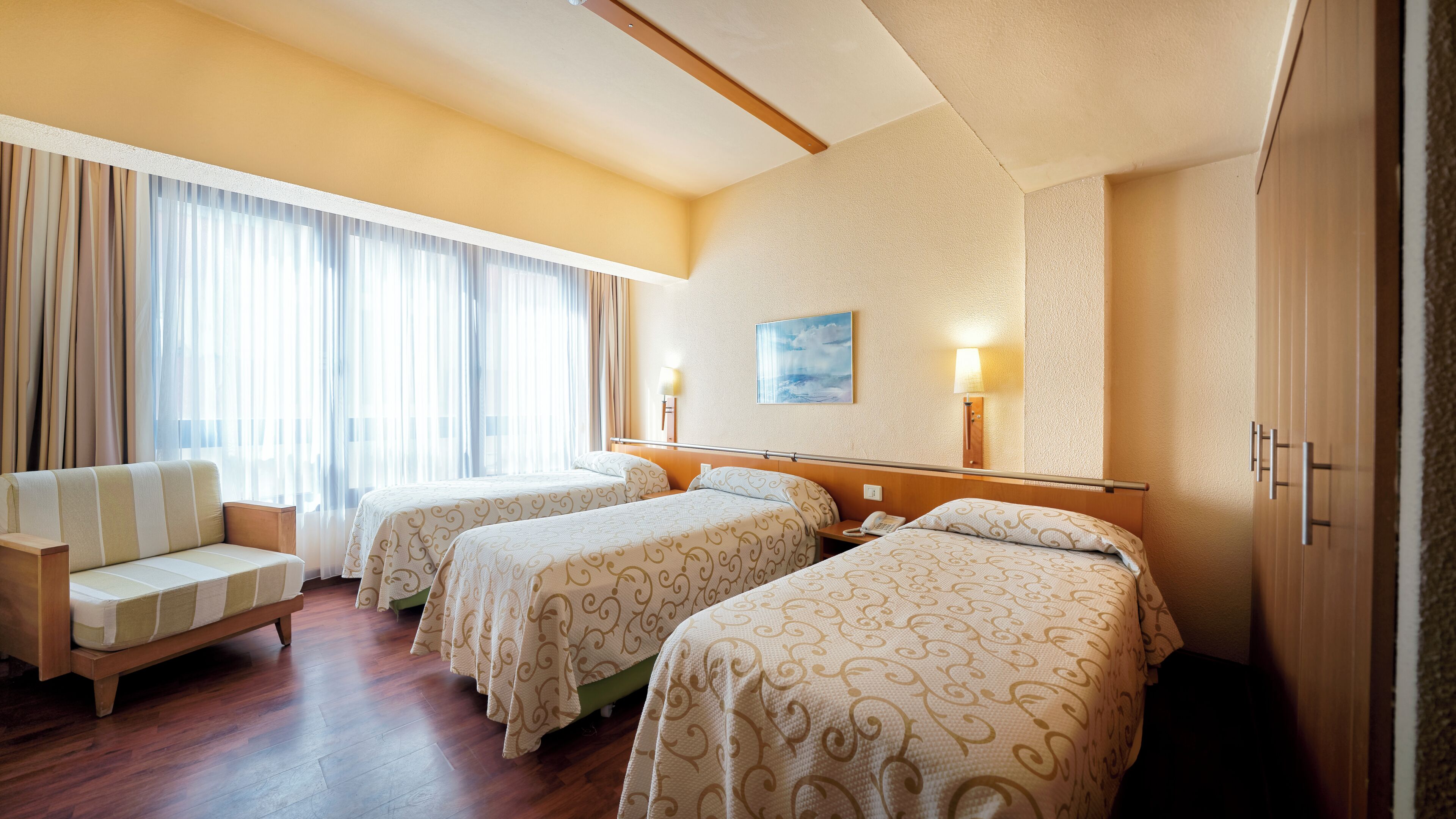 Habitación de hotel con dos camas, un sofá, una lámpara y un cuadro en la pared.