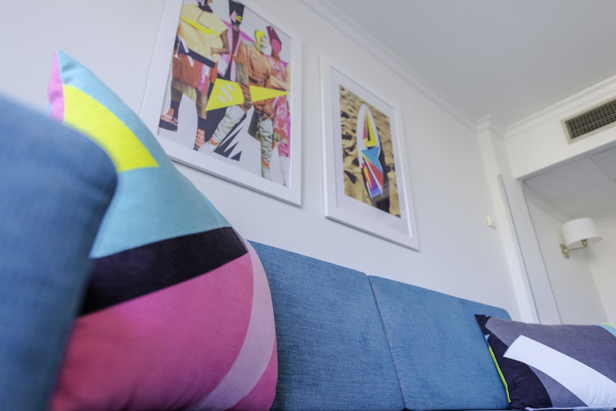 A teal sofa with colorful pillows and two framed abstract paintings on the wall.
