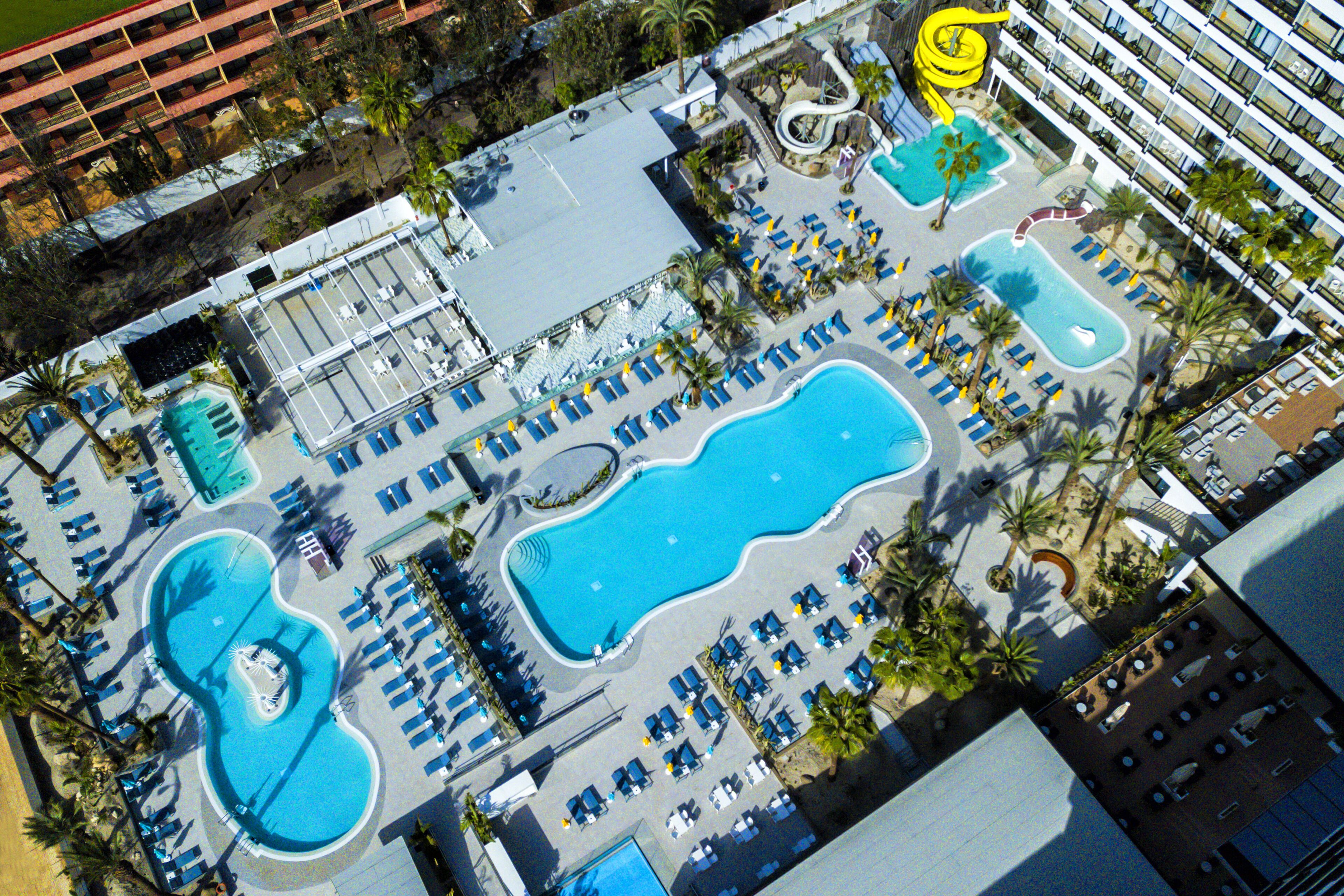 Vista aérea de un hotel con varias piscinas, tumbonas y un tobogán de agua.