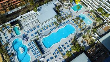 Vista aérea de un hotel con varias piscinas, tumbonas y un tobogán de agua.