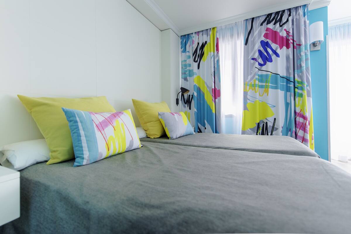 A bedroom with a bed, pillows, and a colorful curtain.