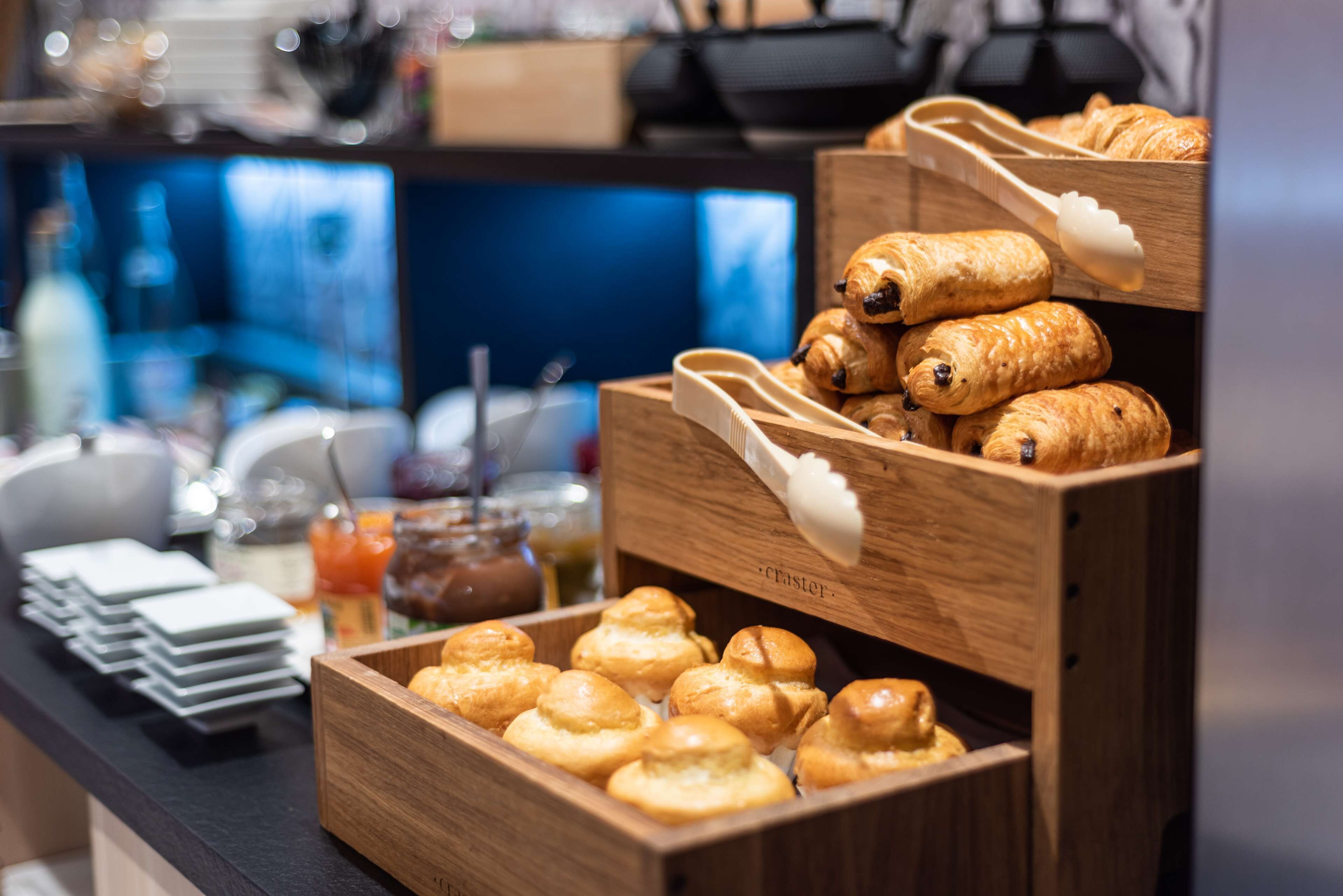 Un bufé con diversas opciones de panadería, incluyendo cruasanes y muffins, dispuestas en cajas de madera.
