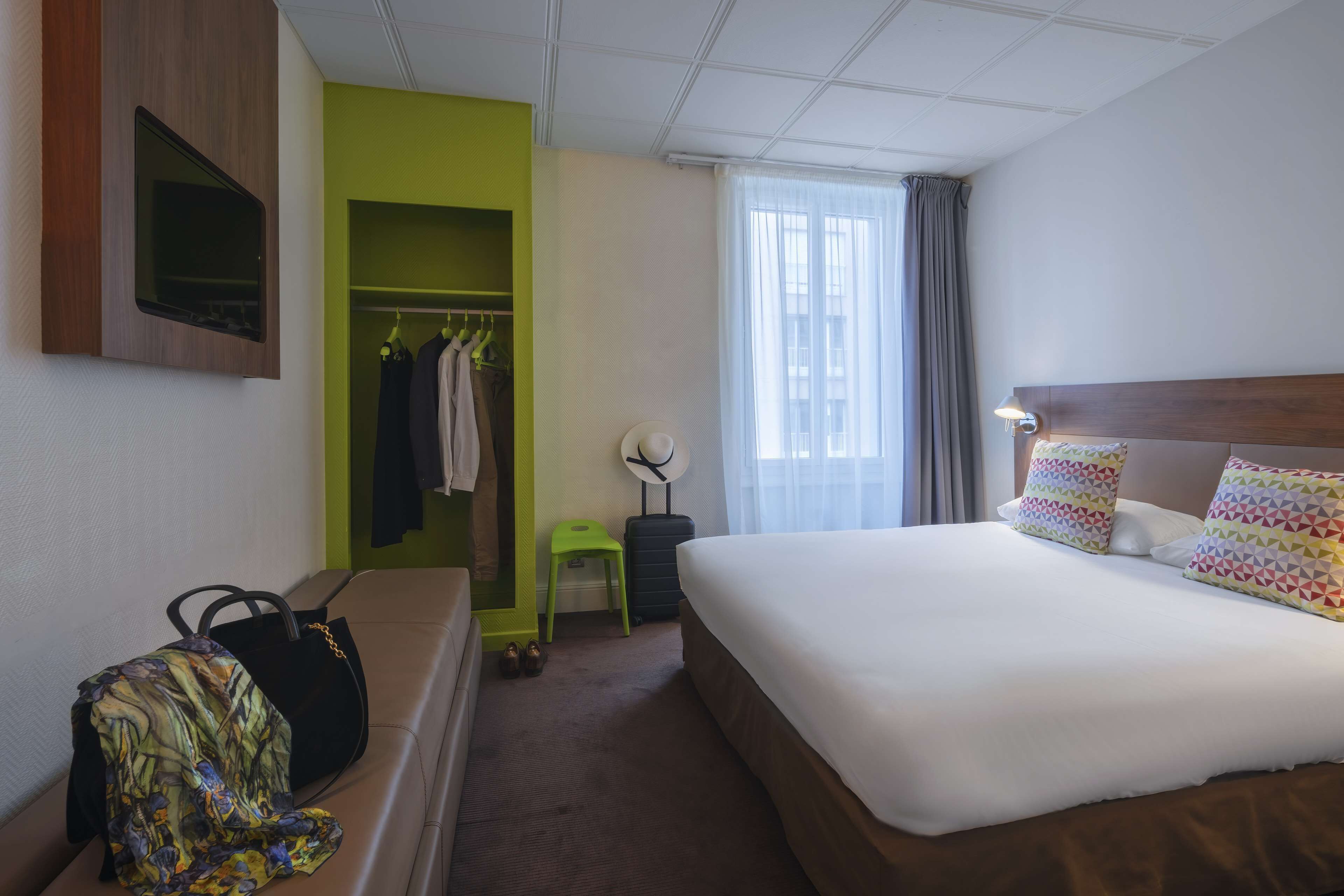 A hotel room with a bed, a desk, a chair, a wardrobe, and a window with curtains.