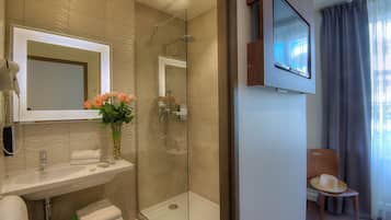A modern bathroom with a glass-enclosed shower, a sink with a mirror, and a chair with a hat.