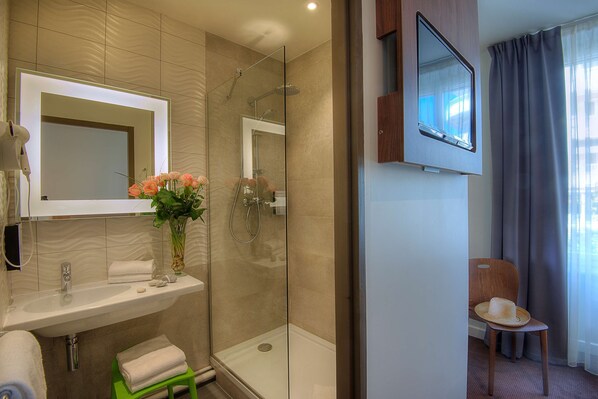 Un baño moderno con ducha de vidrio, lavamanos con espejo y una silla con sombrero.