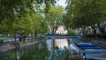 Un río tranquilo con barcas amarradas a la derecha, rodeado de árboles y un muro de piedra.