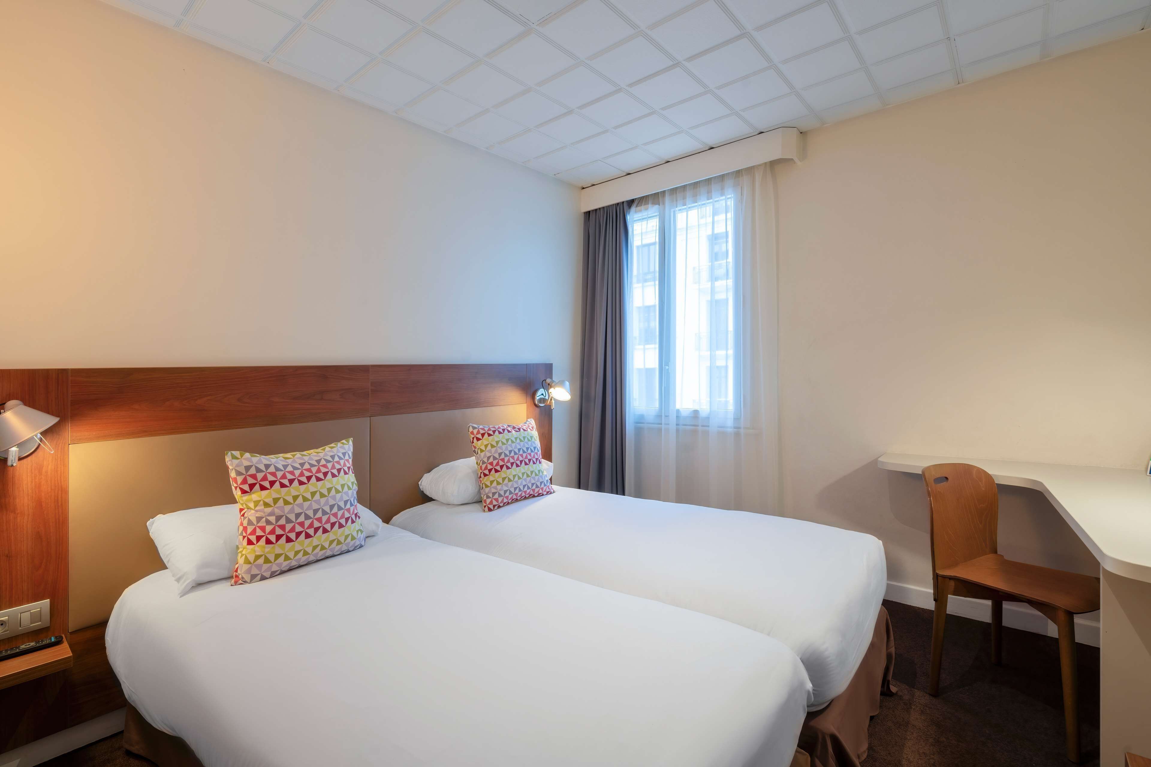 A hotel room with two beds, a desk, and a chair.