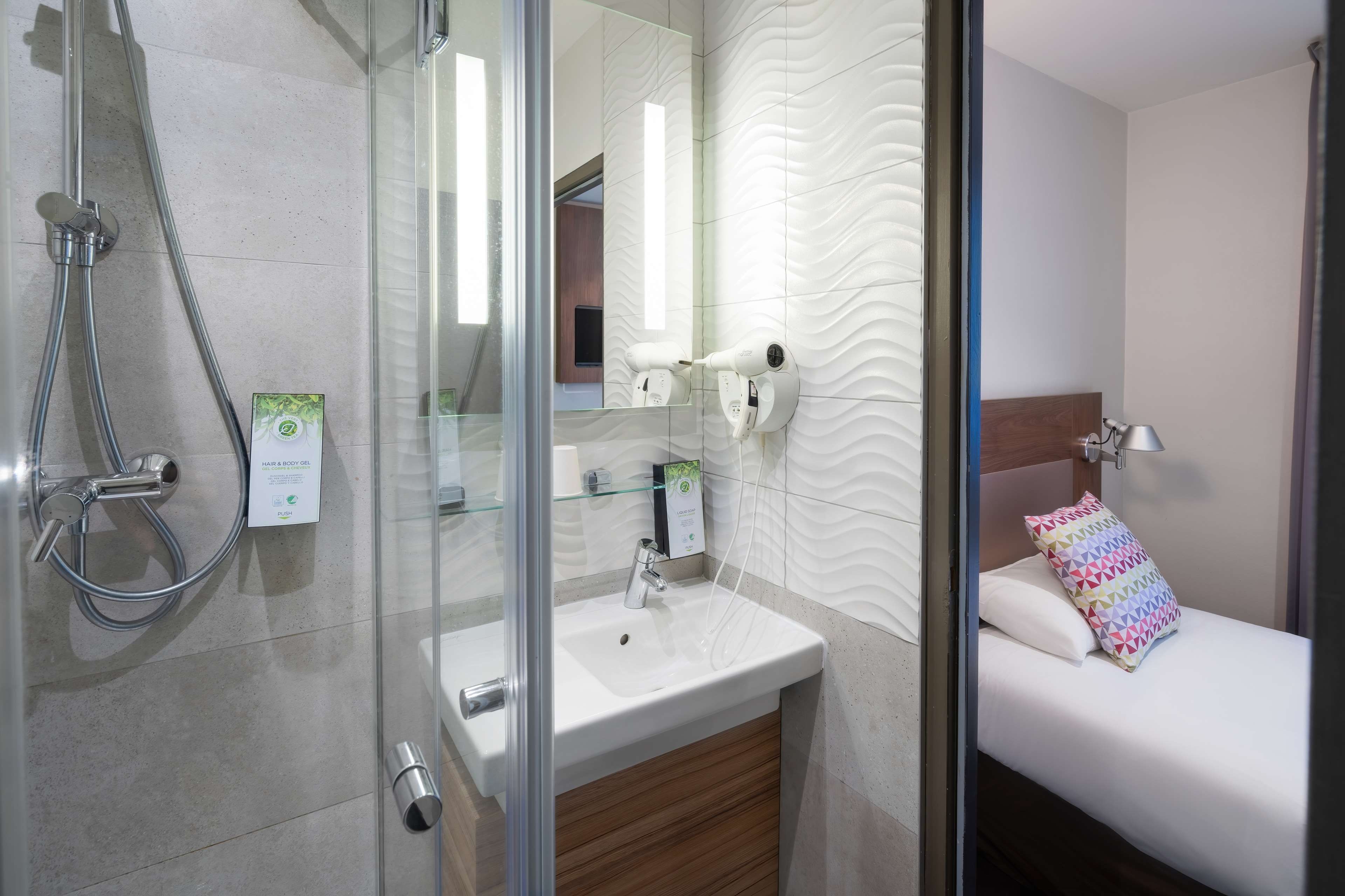Un baño moderno con cabina de ducha de vidrio, un lavamanos blanco y un secador de pelo montado en la pared.