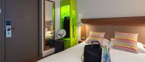 Una habitación de hotel con una cama, un armario verde, un espejo, una mesita de noche y una lámpara de pared.