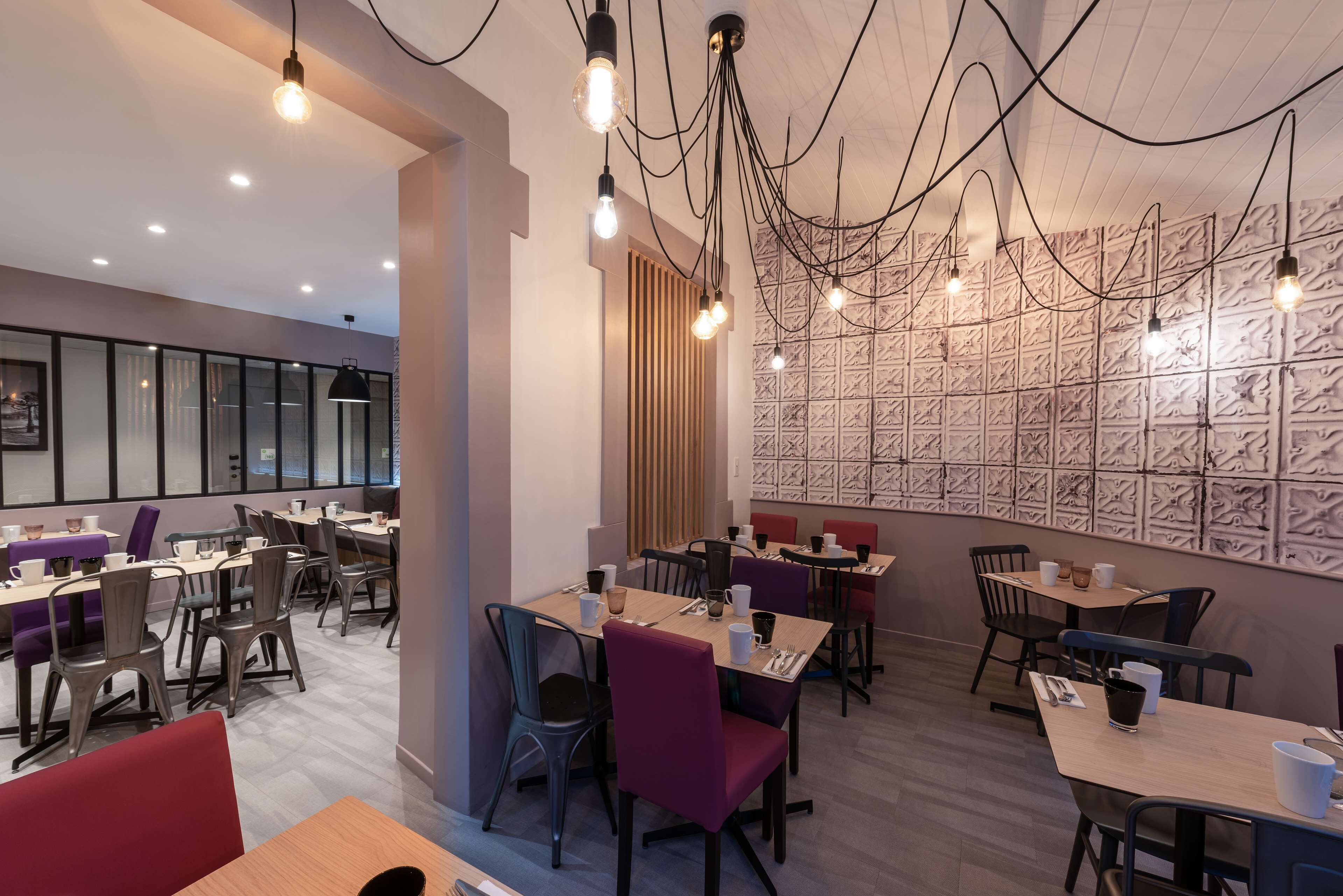 A modern dining area with multiple tables and chairs, pendant lighting, and a textured wall design.