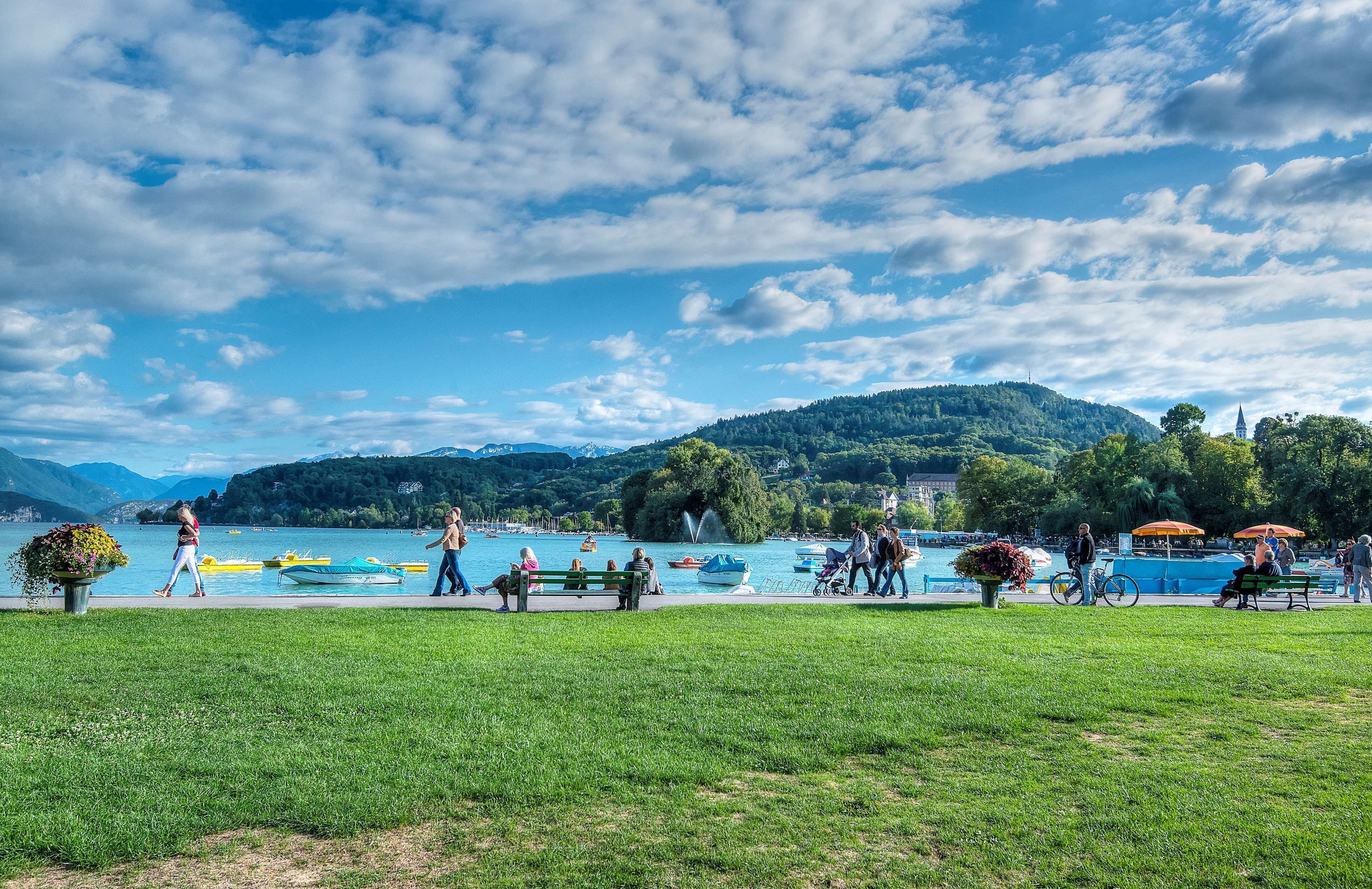 A lakeside park with boats, benches, and people enjoying the scenery.