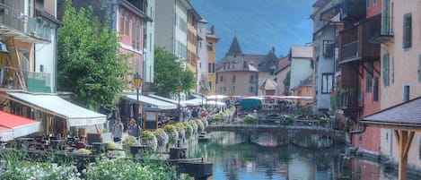 A canal with buildings on either side, a bridge, and mountains in the background.