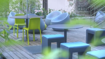 An outdoor seating area with round tables and chairs, surrounded by greenery and a wooden deck.
