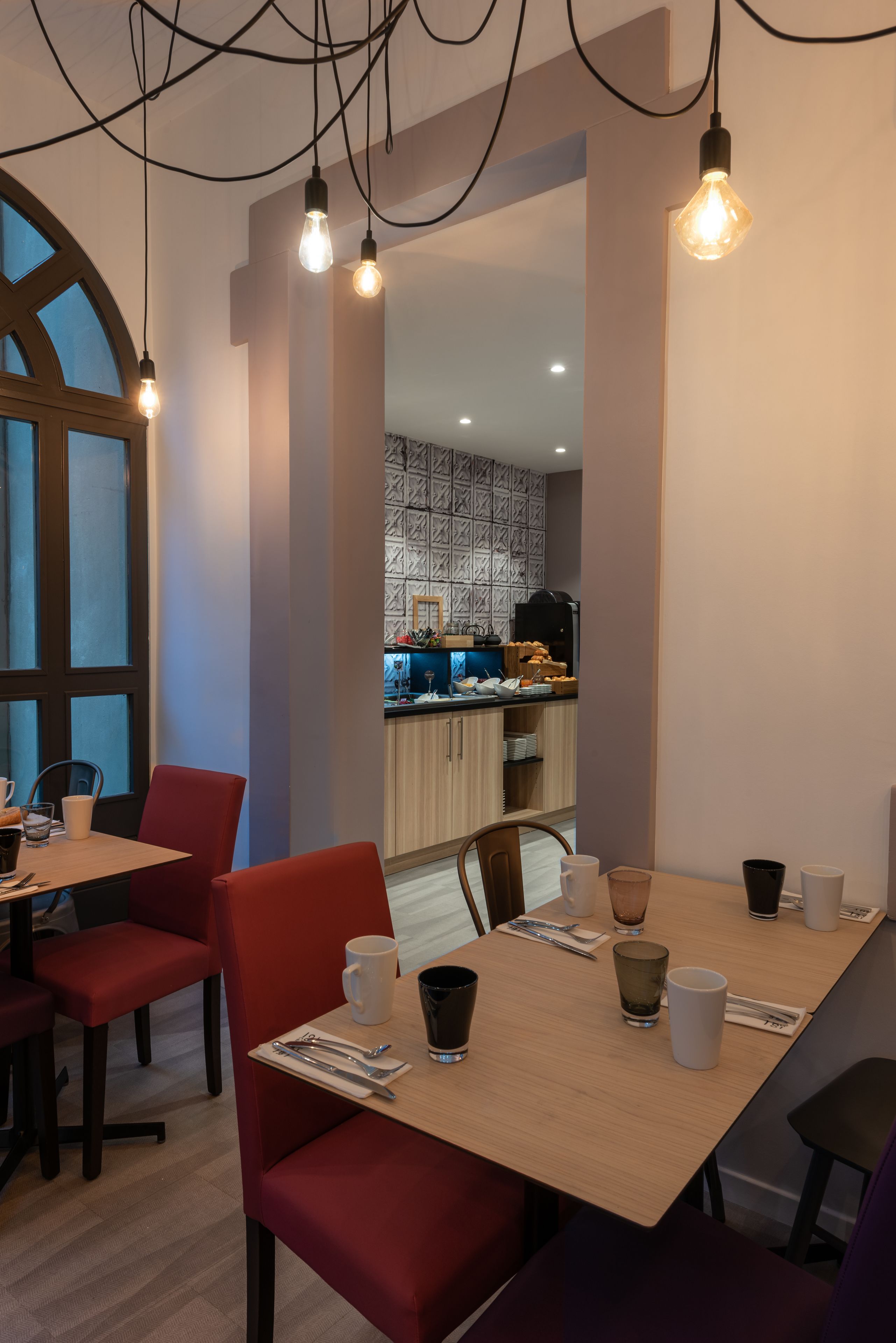 Un comedor moderno con una mesa de madera, sillas rojas y bombillas colgantes.
