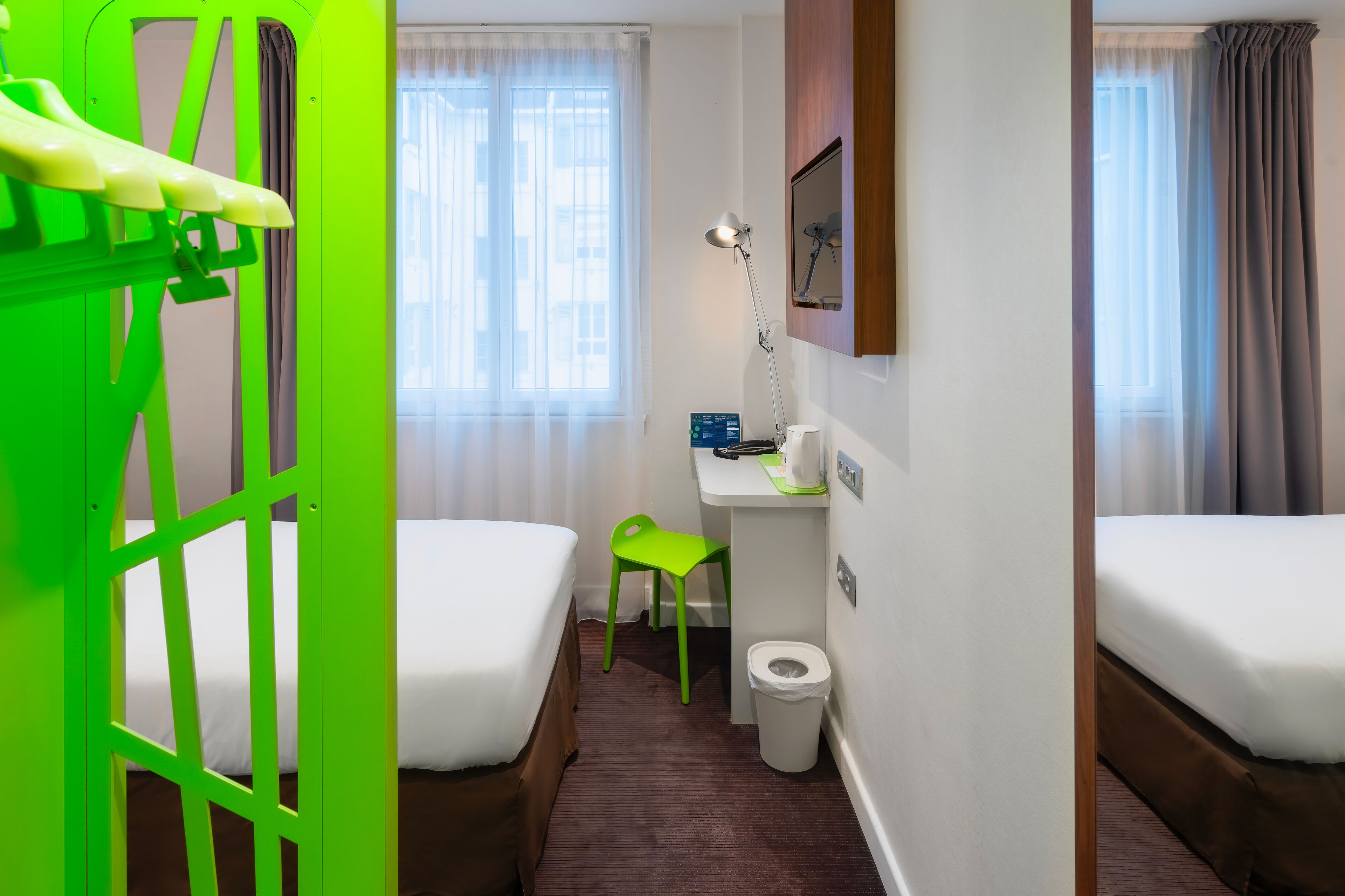A hotel room with two beds, a desk with a chair, a toilet, and a window with curtains.