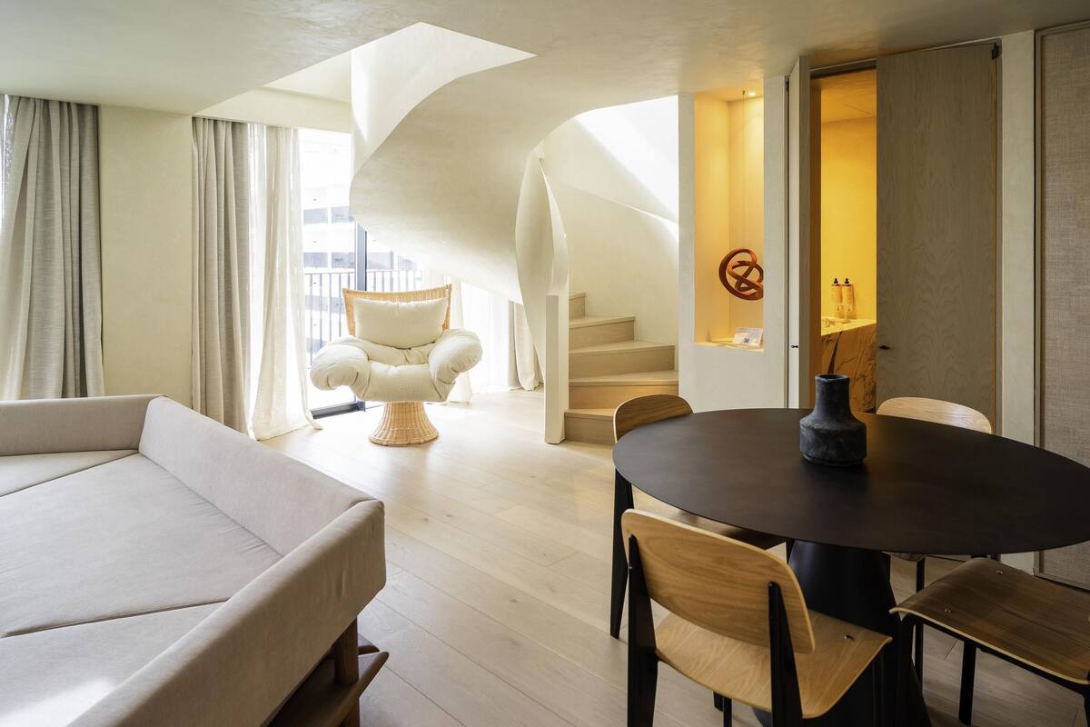 A modern interior with a sofa, dining table, chairs, a wicker chair, and a staircase.
