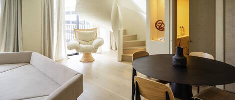 A modern interior with a sofa, dining table, chairs, a wicker chair, and a staircase.