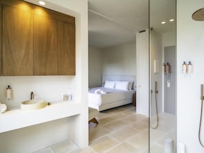A modern bathroom with a wooden vanity, a bed with white linens, and a shower area. - Mercure Benidorm (Benidorm)