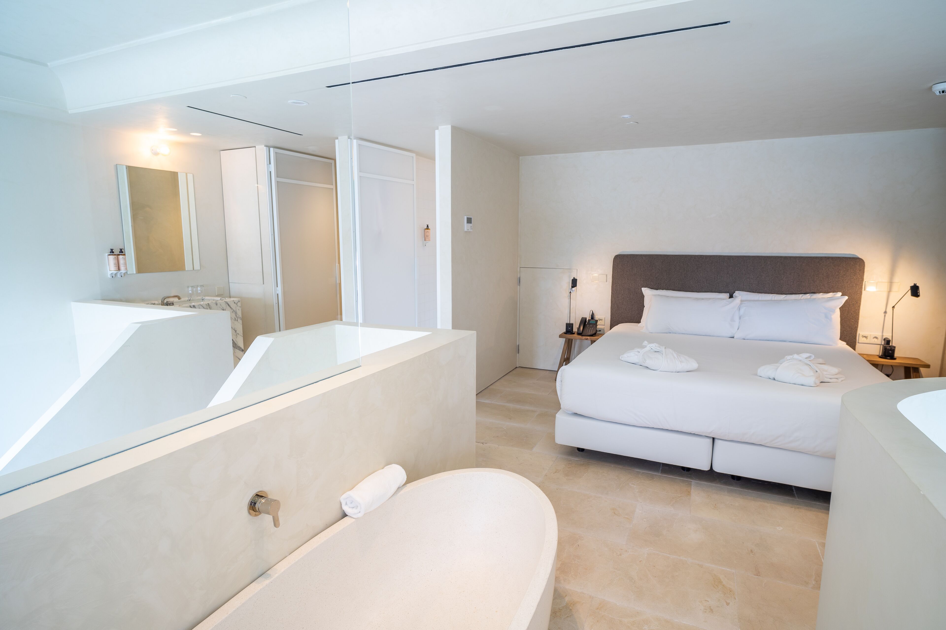 A modern hotel room with a large bed, a separate bathroom with a bathtub, and a large mirror.