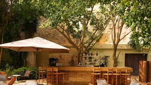 Un espace bar extérieur doté d’un comptoir carrelé, de chaises en osier et d’un grand parasol.