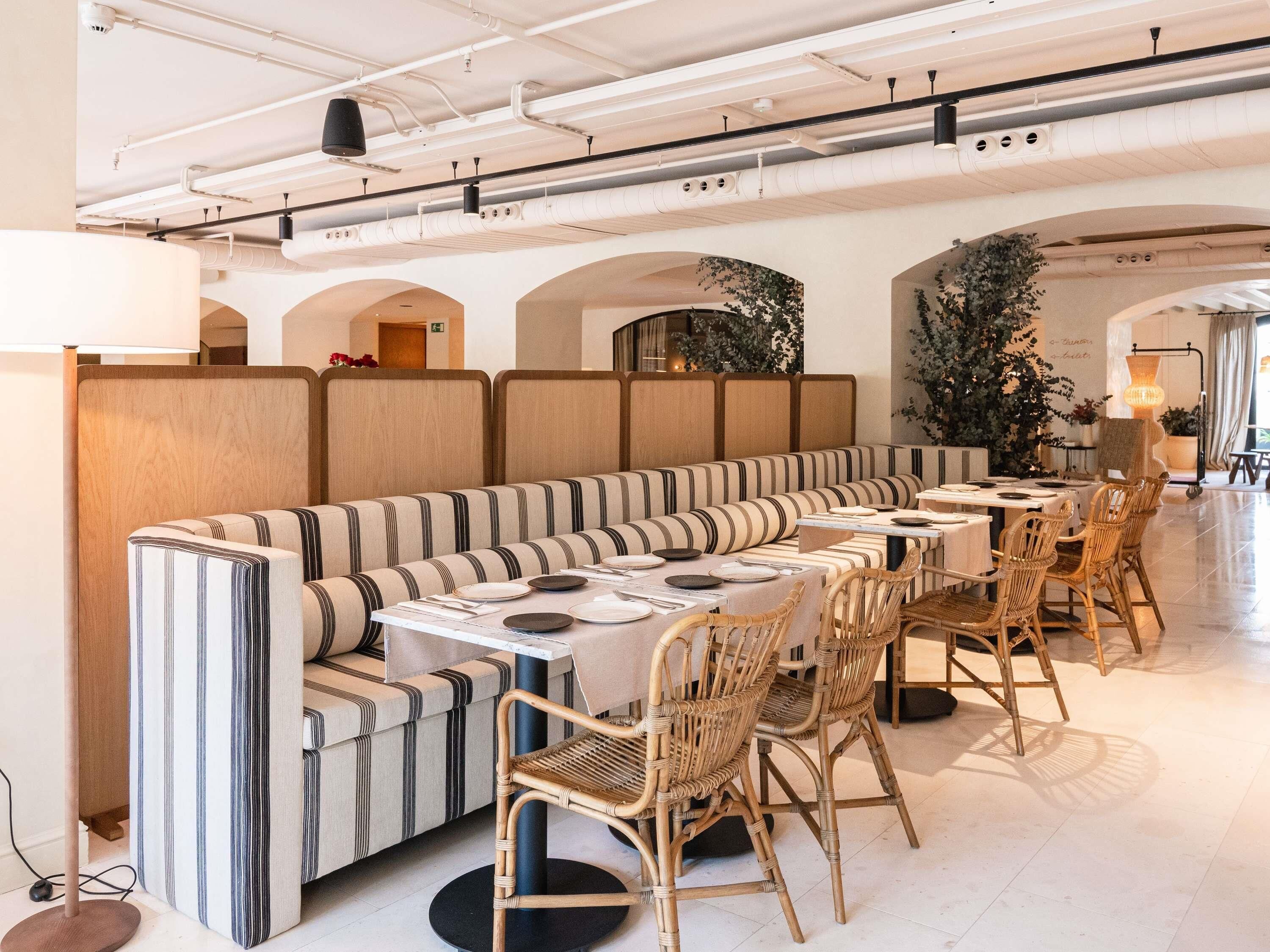 A modern dining area with a long bench and tables, featuring striped upholstery and wicker chairs.