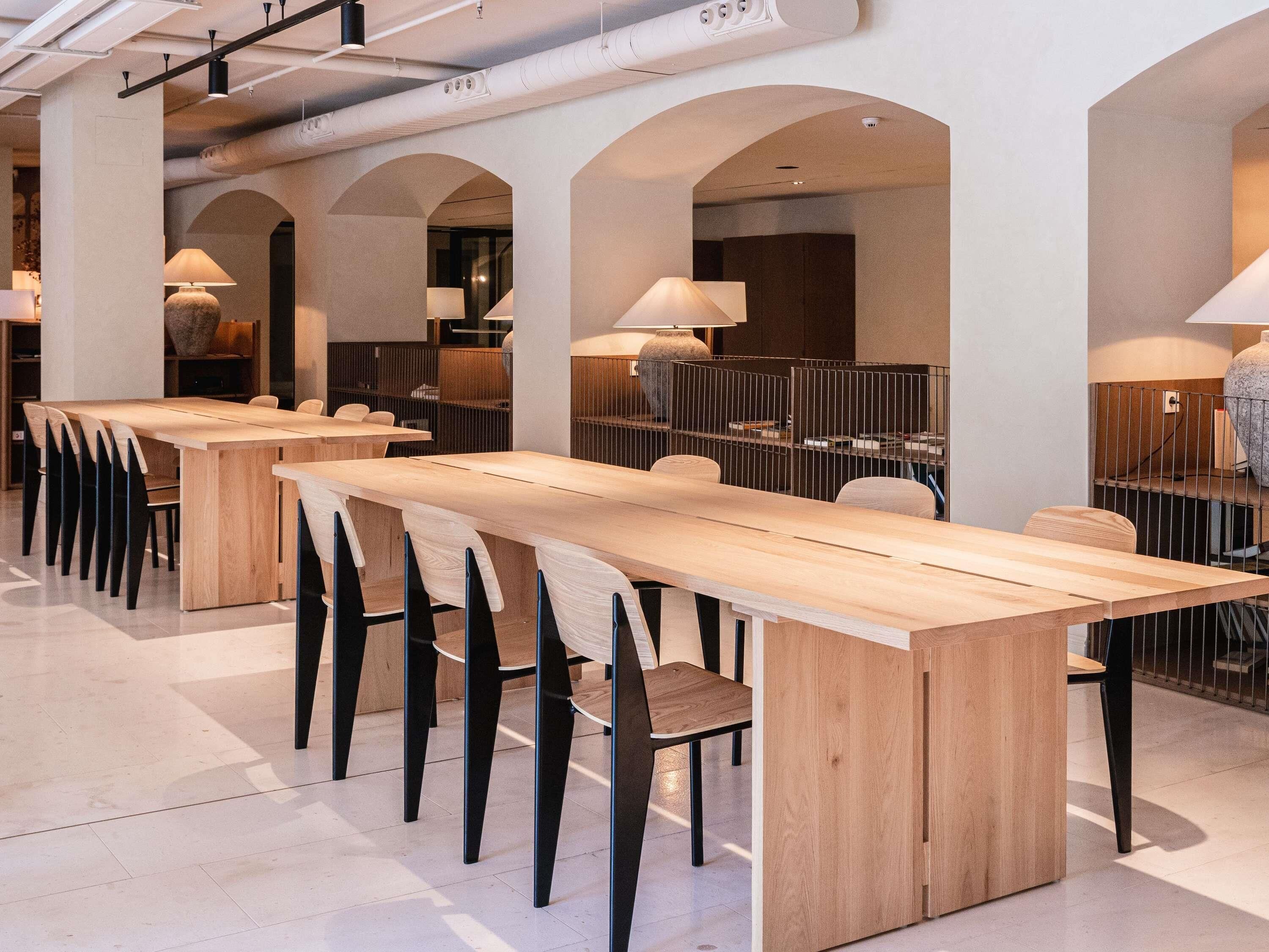 A modern dining area with long wooden tables and black chairs, featuring arched ceilings and pendant lighting.