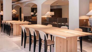 A modern dining area with long wooden tables and black chairs, featuring arched ceilings and pendant lighting.