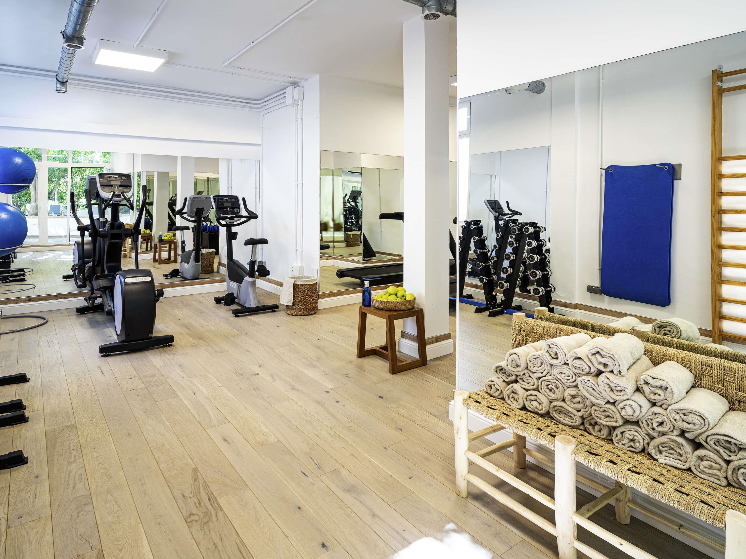 A gym with exercise equipment, wooden flooring, and a mirror reflecting the space.