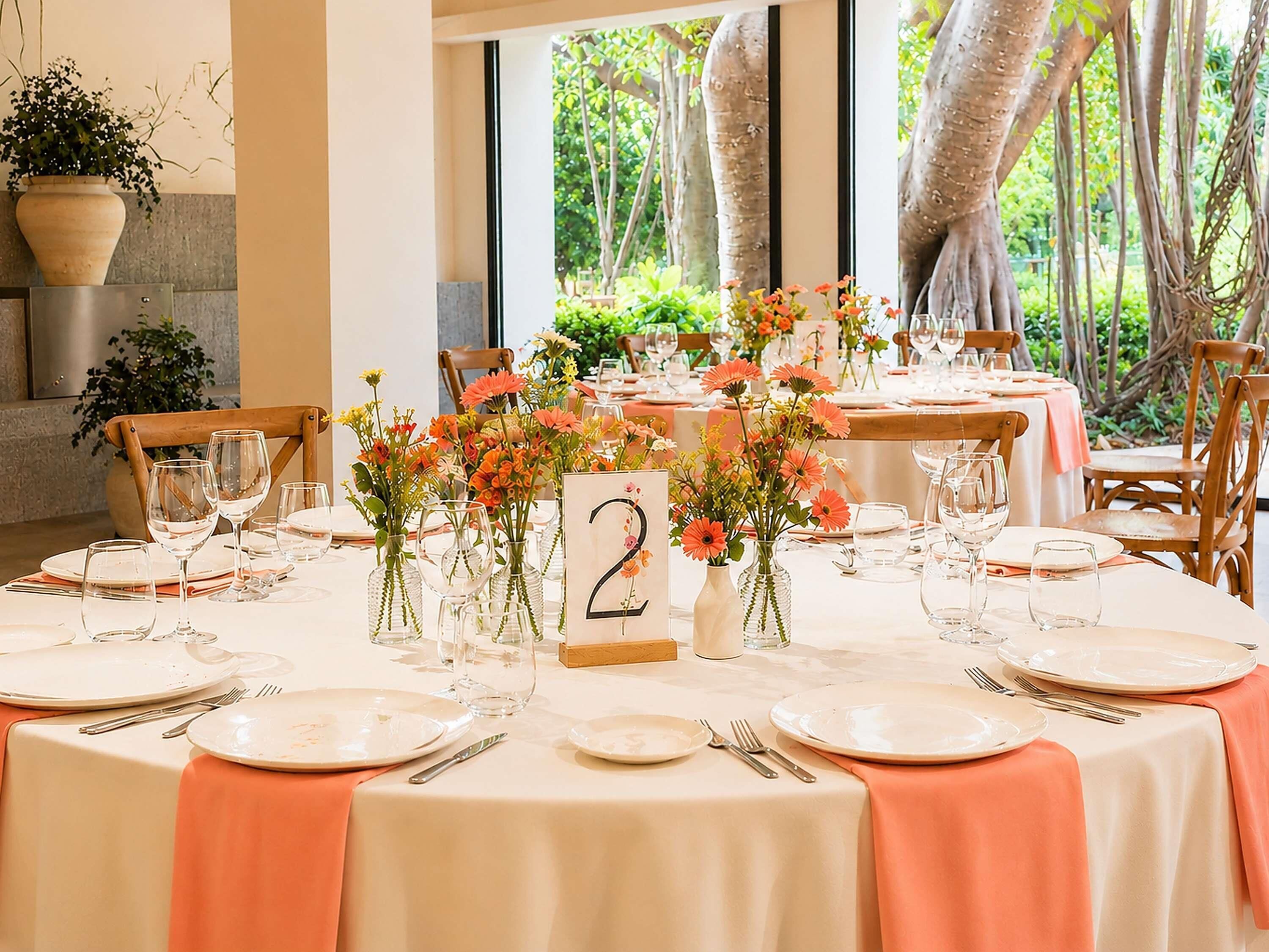 Un comedor con mesas dispuestas para comer, letreros numerados y plantas en macetas.