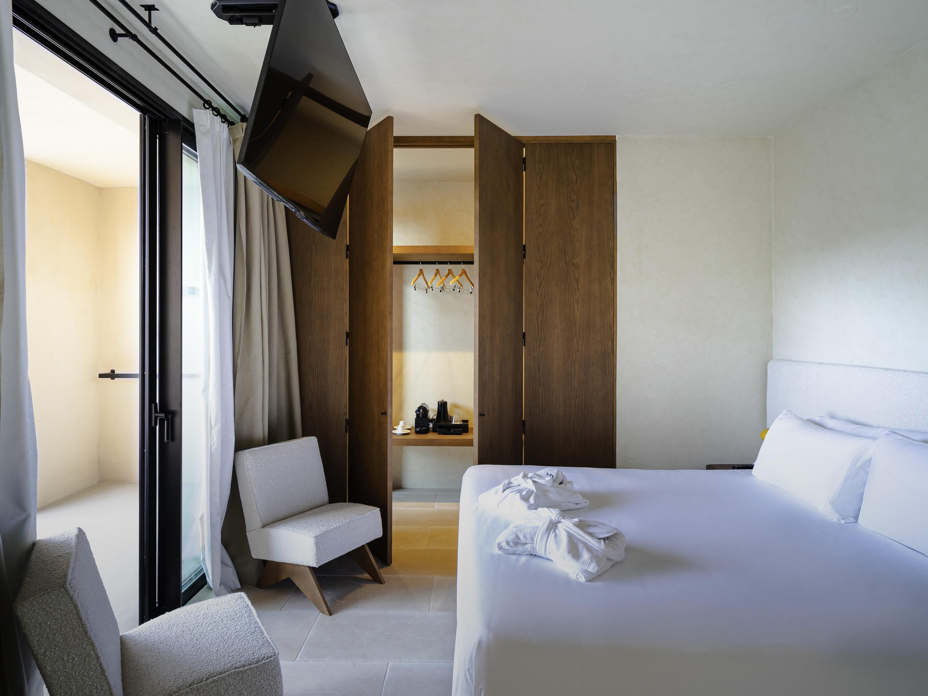 A hotel room with a bed, a chair, a desk with a coffee maker, and a bathroom visible through an open door.