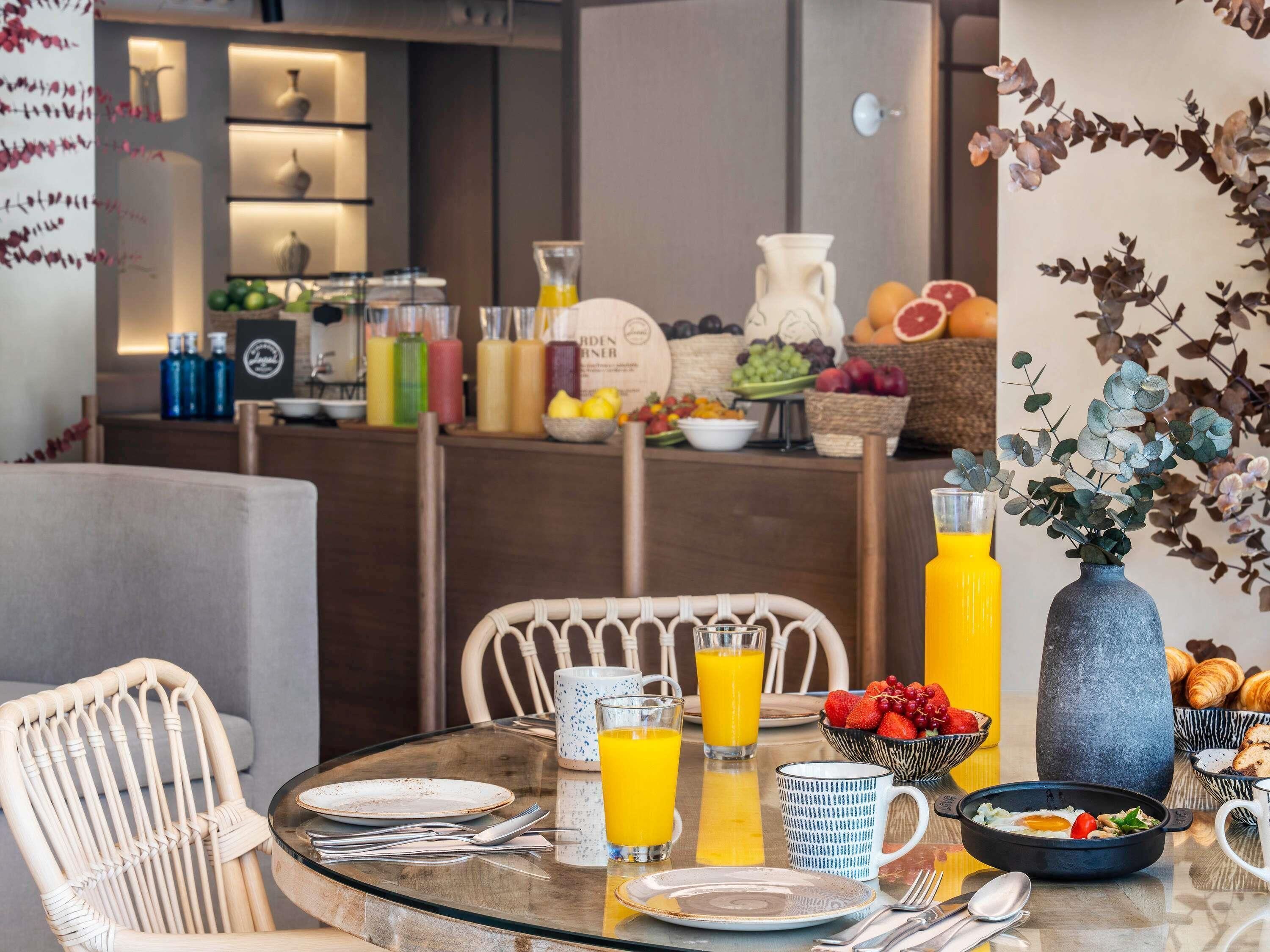 A breakfast setting with a glass table, wicker chairs, and a variety of breakfast items including fruits, eggs, and juice.