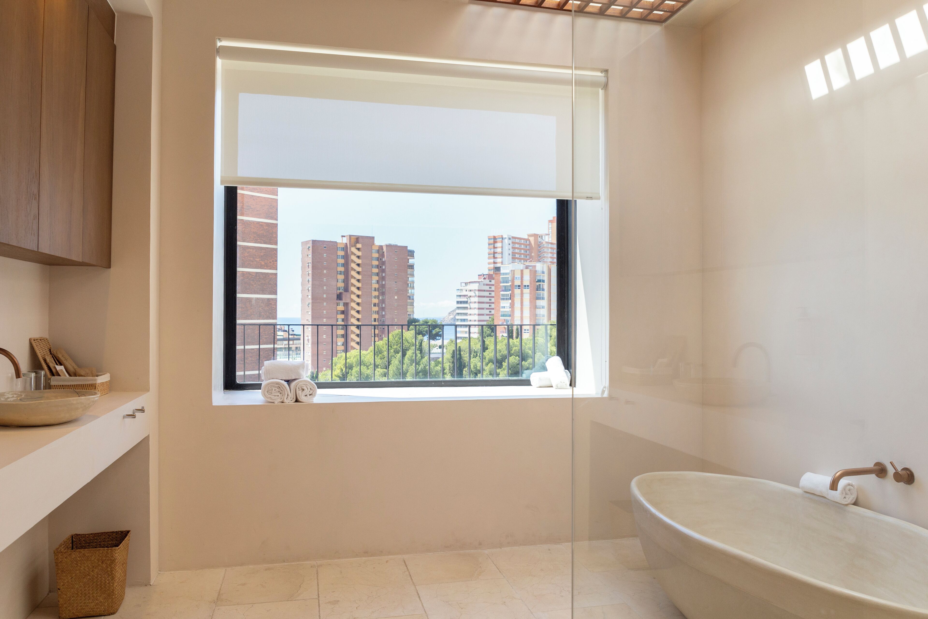 Un baño moderno con un ventanal grande, una bañera independiente y vistas a edificios altos.
