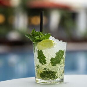 A glass of iced beverage with mint leaves and a slice of lime, placed on a table by a pool. - Mercure Benidorm (Benidorm)