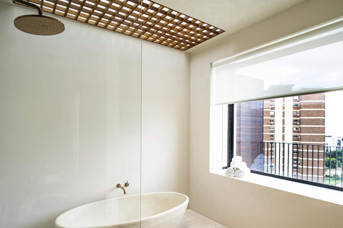 A bathroom with a freestanding bathtub, a showerhead, and a window with a view of buildings.
