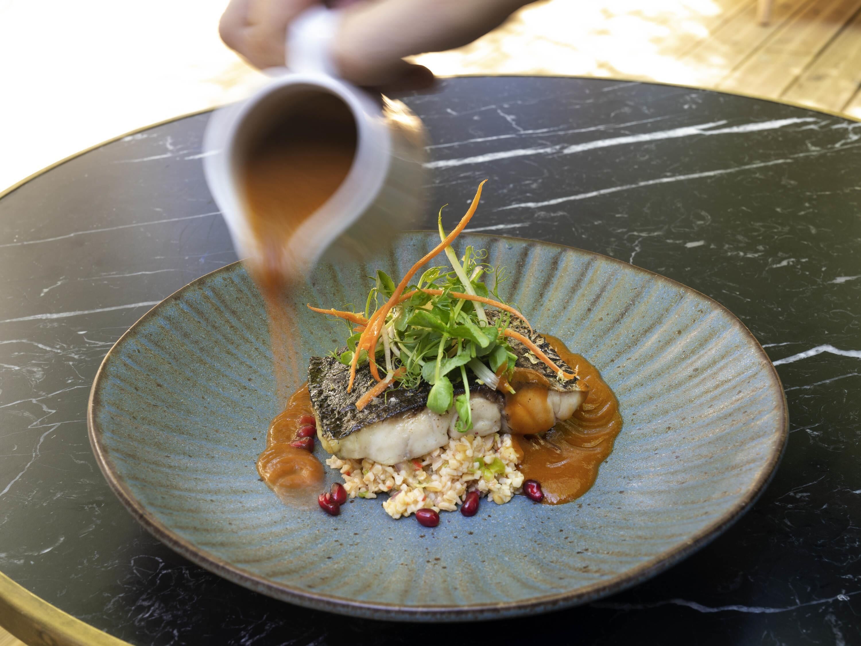 Une assiette contenant du poisson, des légumes, des céréales et une sauce.