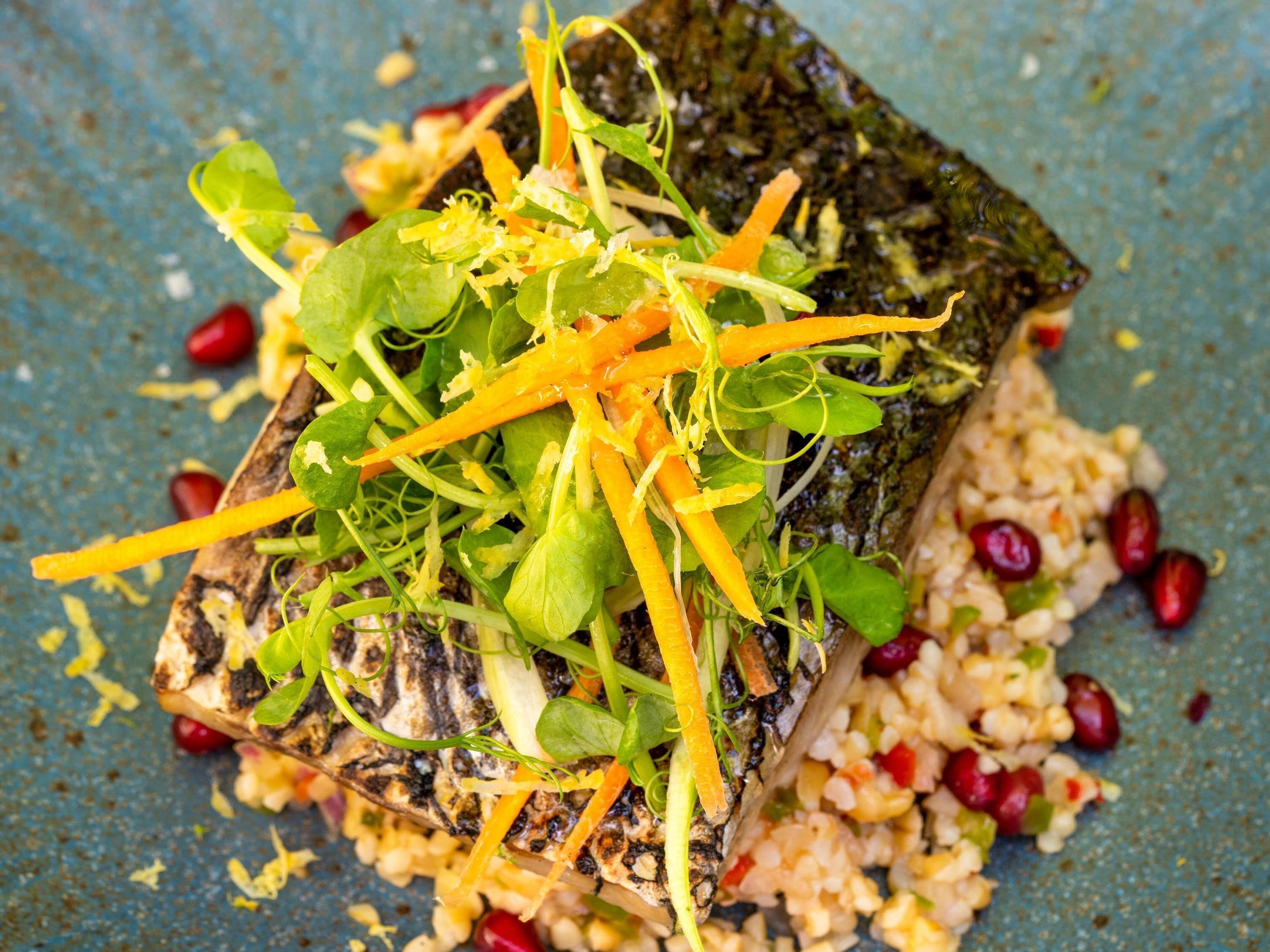 A dish with grilled fish, greens, and shredded carrots on a blue plate.