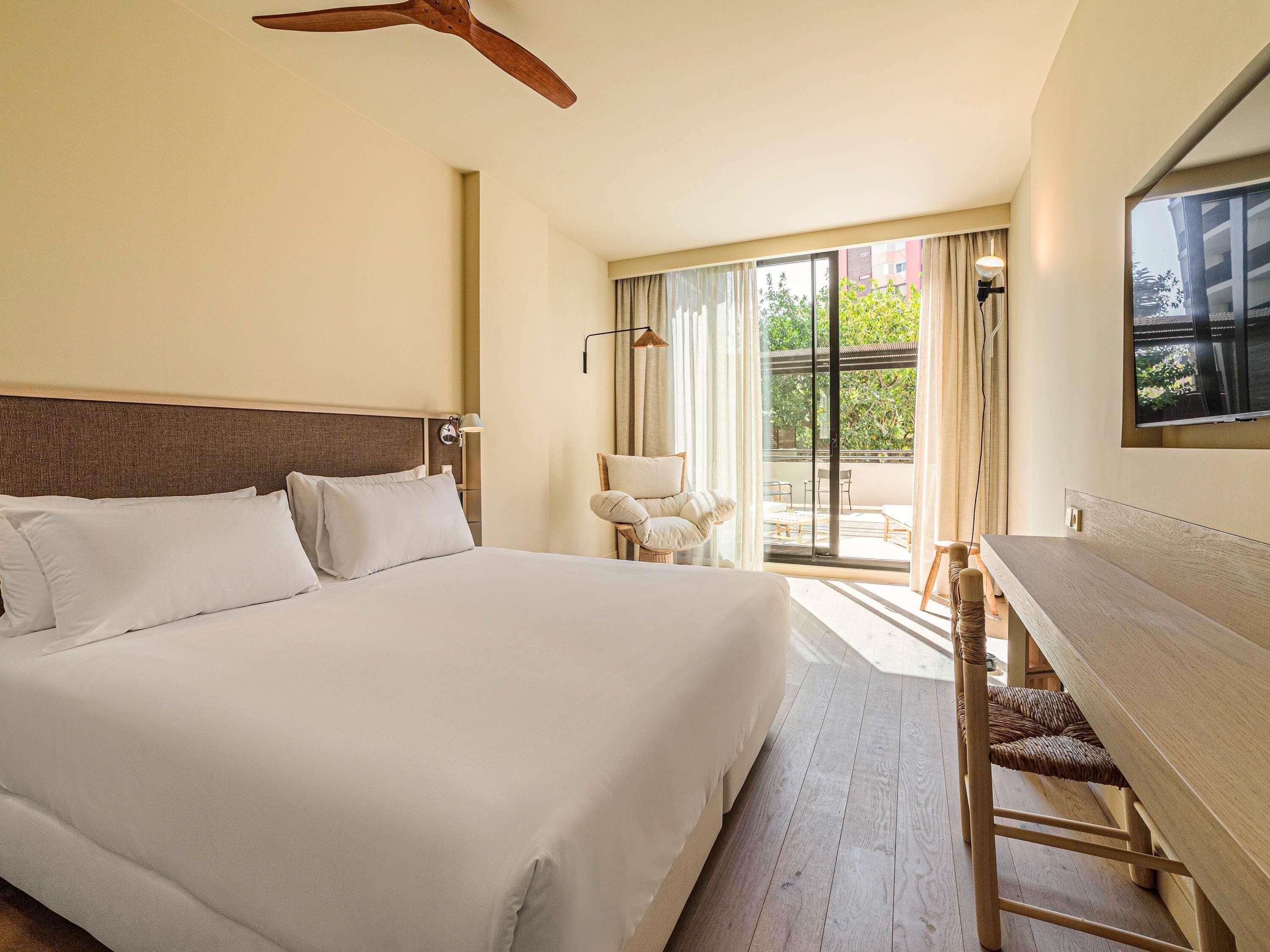 Habitación de hotel con una cama grande, un escritorio, una silla, un ventilador de techo y vistas al exterior.