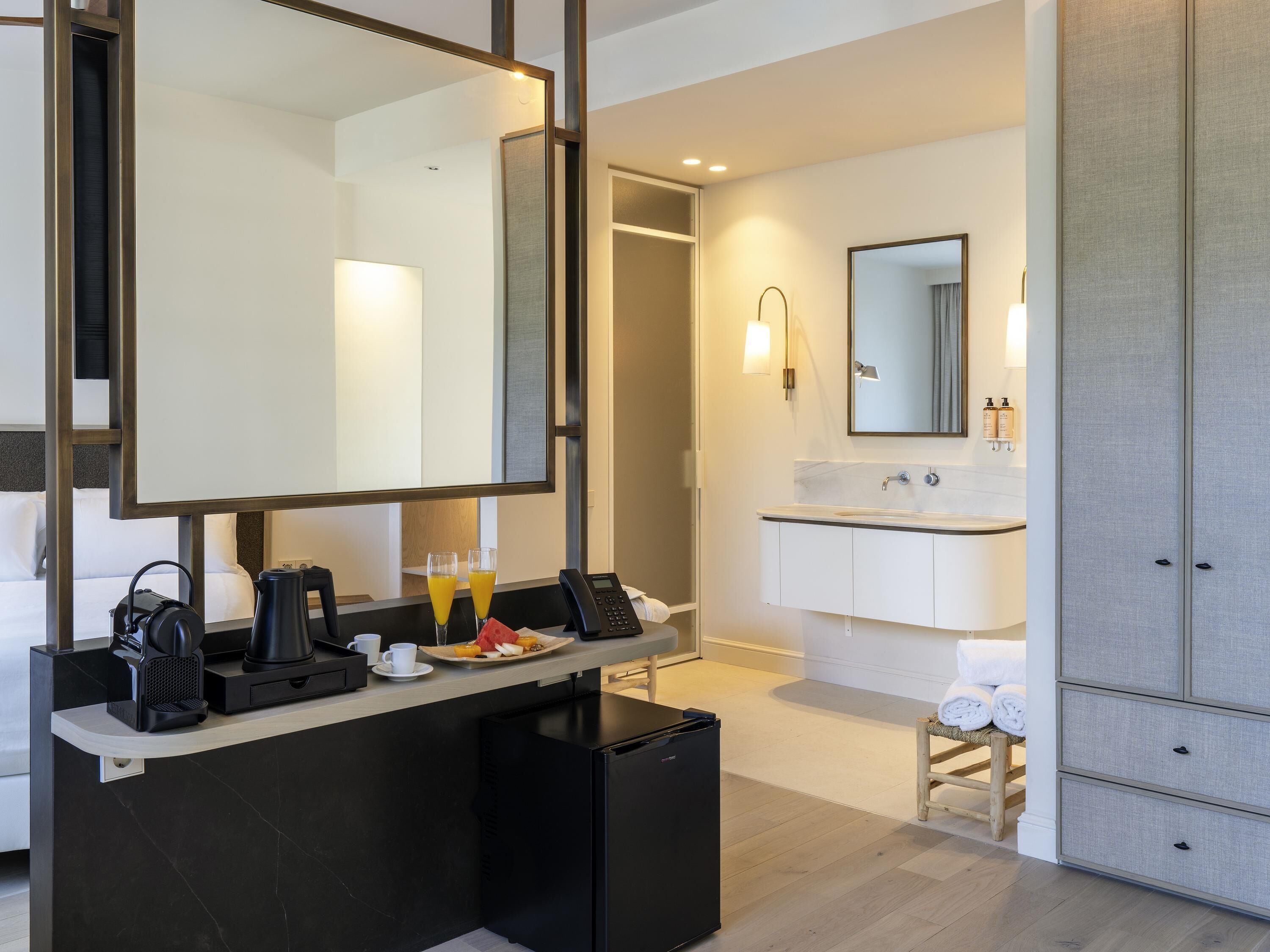 Une salle de bain d’hôtel moderne, dotée d’un grand miroir, d’un lavabo et d’un petit réfrigérateur.